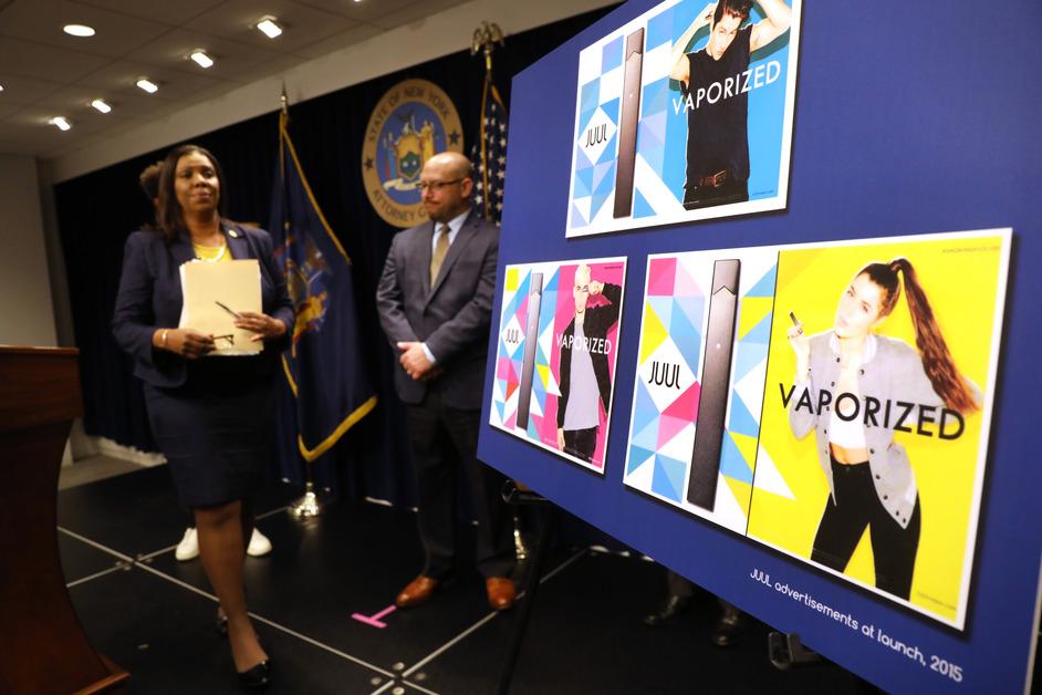 A woman walks in front of a board displaying Juul ads that feature younger people. 